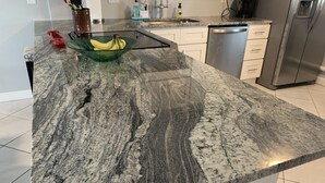 A kitchen with a granite countertop, a glass bowl with bananas, a coffee maker, and a dishwasher. - Beachfront condo with direct pool & ocean view on St Augustine Beach (St Augustine Beach)