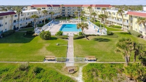 A hotel with a central swimming pool, multiple balconies, and a well-maintained lawn. - Beachfront condo with direct pool & ocean view on St Augustine Beach (St Augustine Beach)