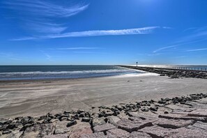 Une plage avec un rivage rocheux au premier plan, une étendue de sable et une jetée qui s’avance dans l’eau.