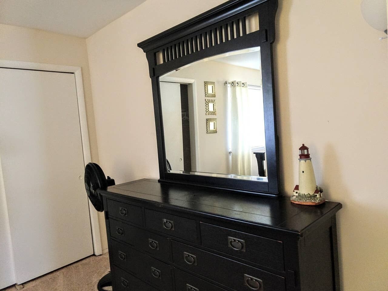 A dark wooden dresser with a mirror above it, a small decorative lighthouse, and a white door in the background.