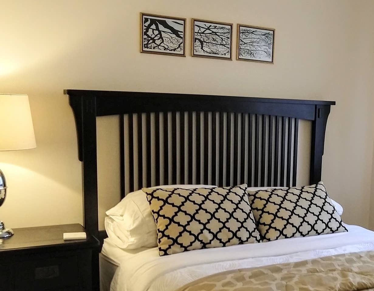 A hotel room with a bed, a nightstand, a lamp, and three framed pictures on the wall.