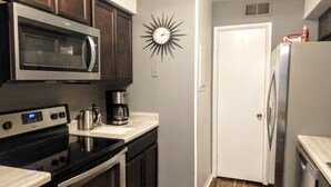 Uma cozinha compacta com micro-ondas, fogão, cafeteira e um relógio de parede com design solar.