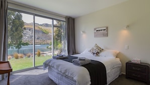 Een slaapkamer met een groot bed, uitzicht op een meer en een klein tafeltje met een stoel.