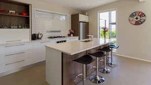 Een moderne keuken met een centraal eiland, barstoelen, een groot raam en een decoratieve klok aan de muur.