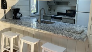 A kitchen with white cabinets, a granite countertop, a sink, a stove, and three white stools. - Middlesex Beach - Sunday to Sunday summer rentals.  Private community beach.  (Bethany Beach)