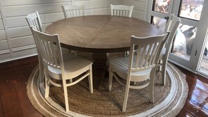 A round wooden dining table with six white chairs, surrounded by a woven rug, in a room with wooden walls and a glass door leading outside. - Middlesex Beach - Sunday to Sunday summer rentals.  Private community beach.  (Bethany Beach)