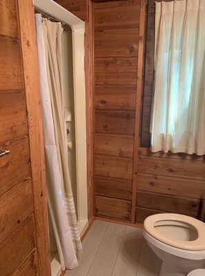 A wooden-paneled bathroom with a shower curtain, a toilet, and a window with a curtain. - Middlesex Beach - Sunday to Sunday summer rentals.  Private community beach.  (Bethany Beach)