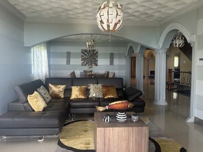 A modern living room with a sectional sofa, decorative pillows, a unique fish sculpture, and a contemporary chandelier. - Luxury, Privacy & Breathtaking Ocean Views Await.” (Westmoreland)