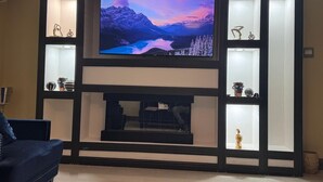 A living room with a large flat-screen TV mounted above a fireplace, surrounded by shelves with decorative items. - Luxury ocean view villa  (Westmoreland)