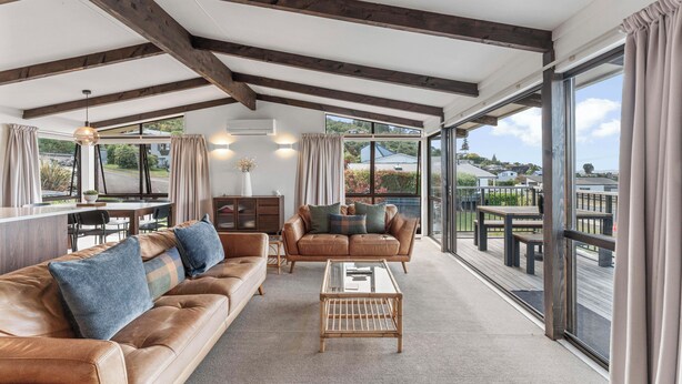 A spacious living area with a leather sofa, a glass coffee table, and a view of a deck and water.