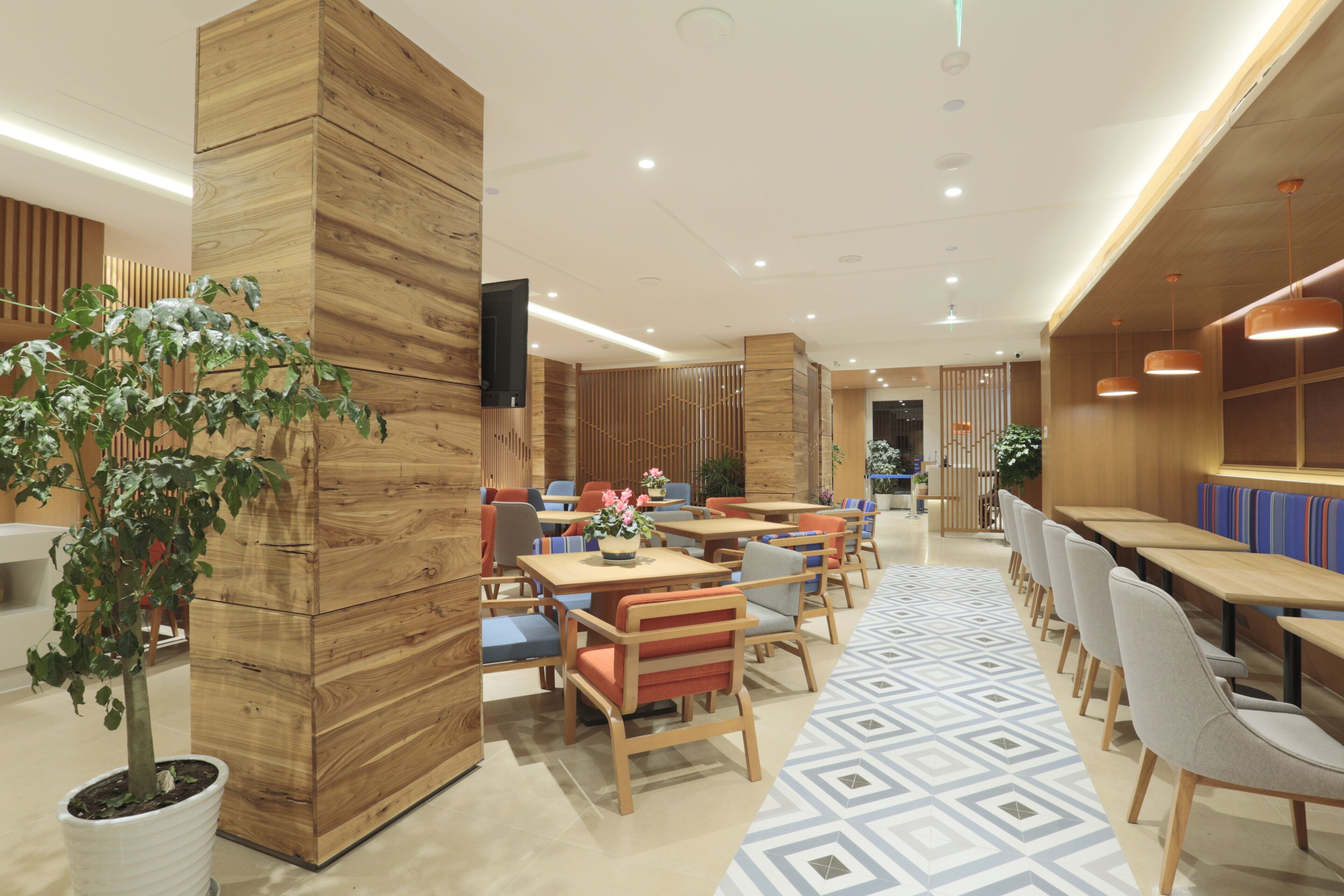 A modern restaurant interior with wooden paneling, multiple seating areas, and a potted plant.