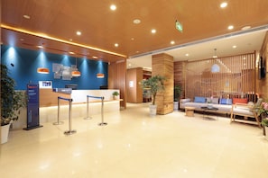 A hotel reception area with a wooden reception desk, a seating area with a sofa and chairs, and a reception counter with a blue backdrop.