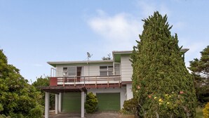 A two-story house with a green garage, a satellite dish, and a well-maintained garden with various plants and flowers. - Holiday Haven - Whitianga Bach (Whitianga)