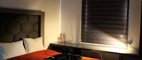 A hotel room with a bed, a nightstand, a lamp, and a window with blinds.