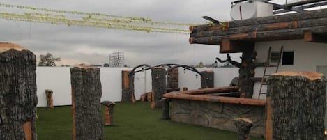 An outdoor area with artificial grass, tree stump seating, and a white building in the background.