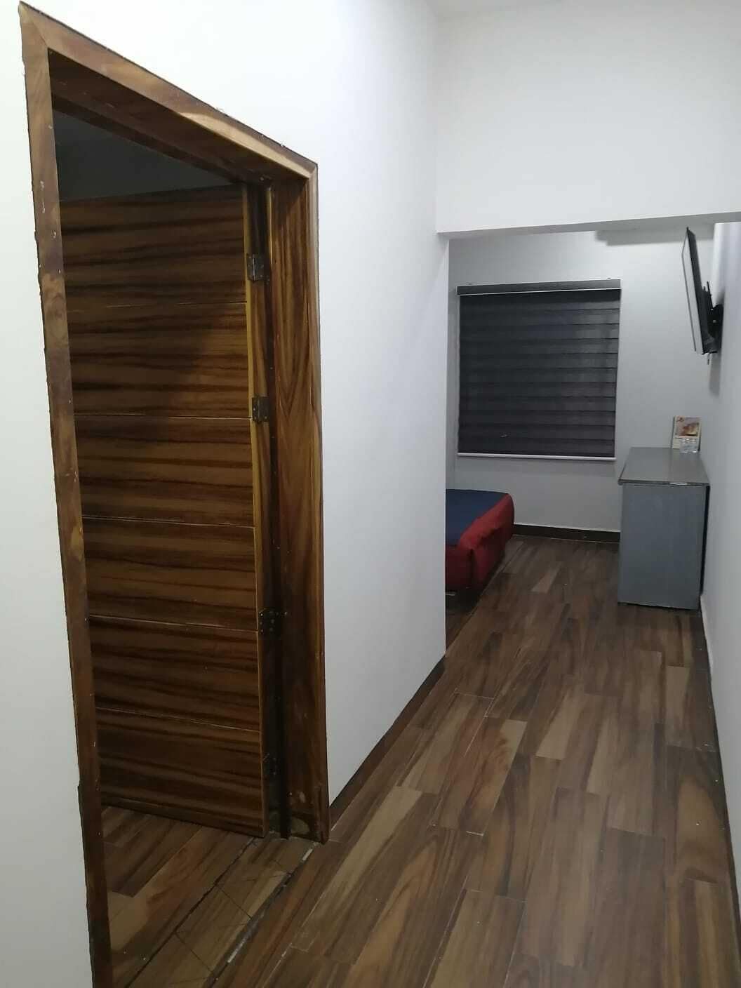 A hallway with a wooden door, a window with blinds, a small red sofa, and a grey cabinet.