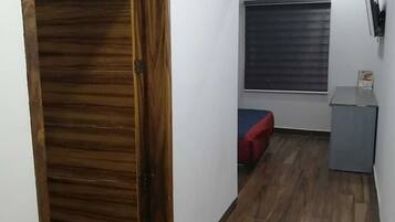 Un pasillo con una puerta de madera, una ventana con persianas, un sofá pequeño rojo y un armario gris.
