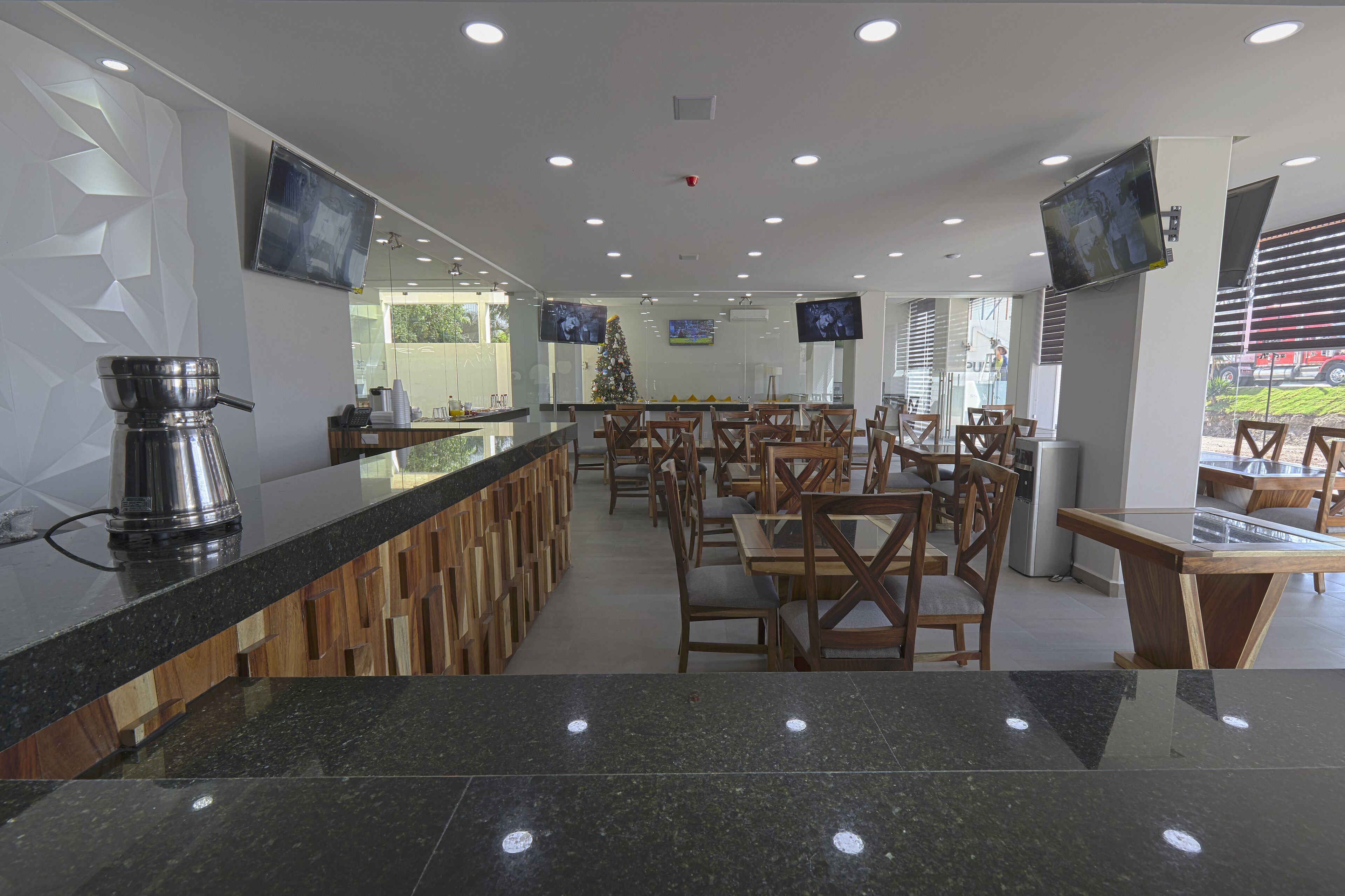 A modern restaurant with a long counter, multiple TVs, and a Christmas tree.