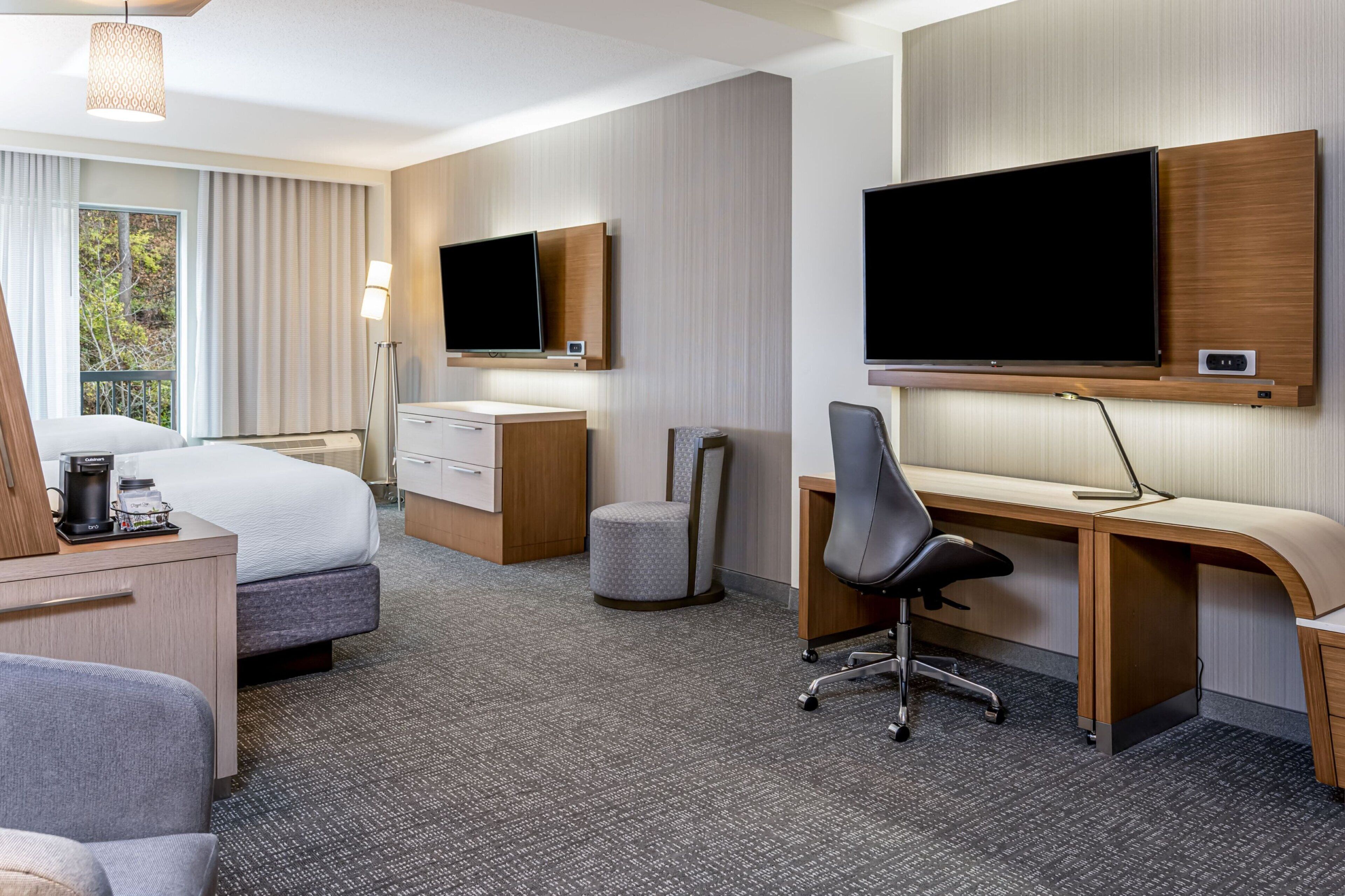 A hotel room with a bed, desk, chair, television, and a window with curtains.