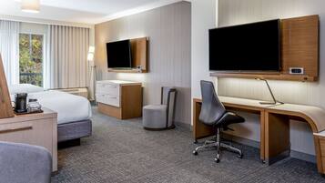 A hotel room with a bed, desk, chair, television, and a window with curtains.