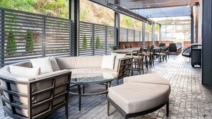 An outdoor patio area with a sofa, tables, and chairs, surrounded by a metal fence and brick walls. - Courtyard by Marriott Asheville Biltmore Village (Asheville)