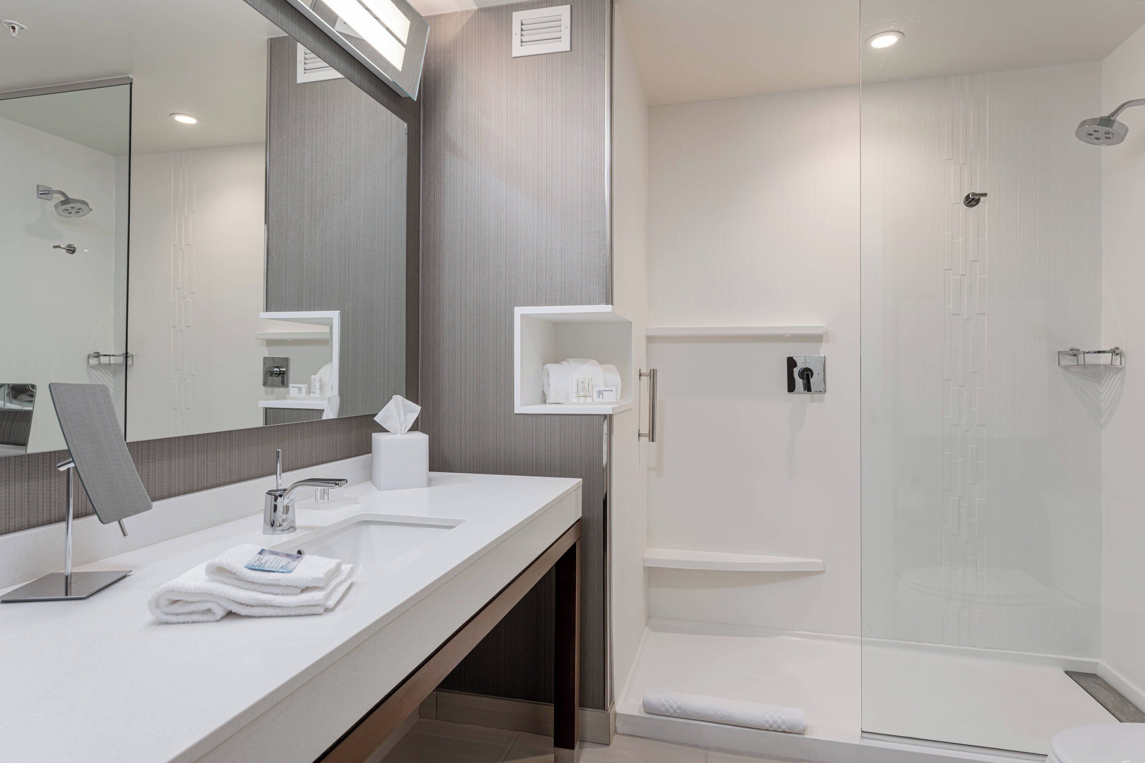 A modern bathroom with a large mirror, a sink, and a shower area.