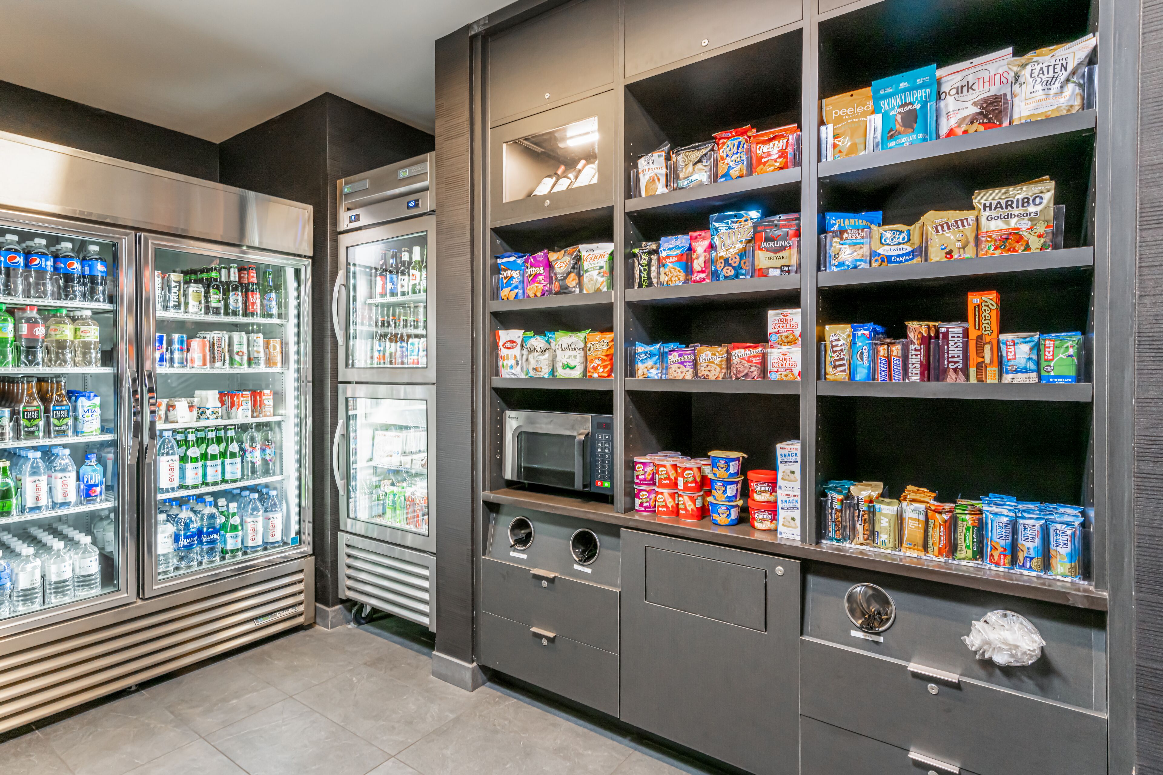 A self-service snack and beverage area with refrigerated drinks, microwaves, and shelves stocked with snacks and cereals.