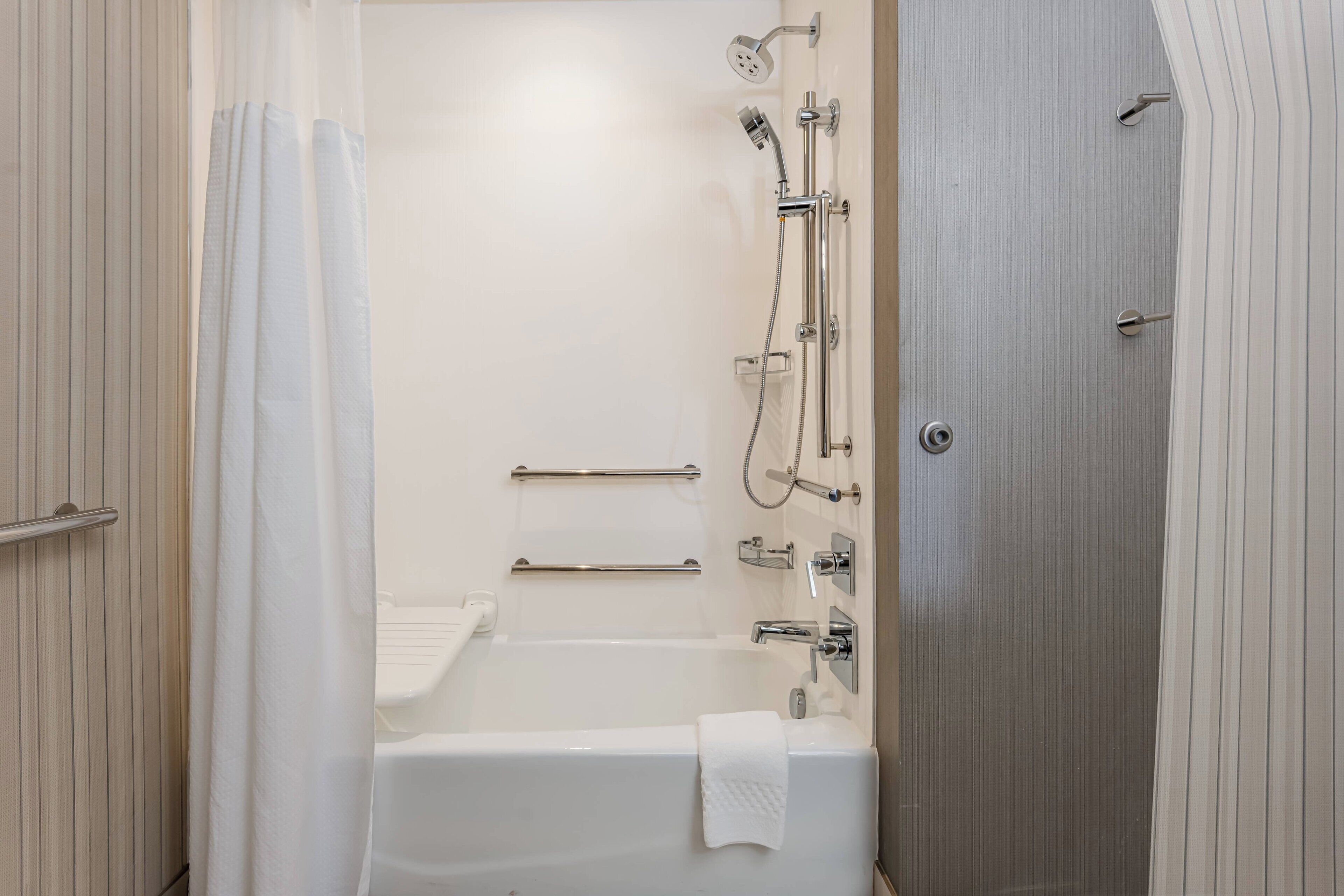 A modern bathroom with a bathtub, shower, and handrails.