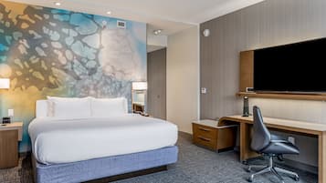 Une chambre d’hôtel dotée d’un grand lit, d’un bureau, d’une chaise, d’un téléviseur à écran plat et d’un mur orné d’un motif abstrait aux couleurs vives.