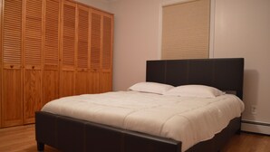 Un dormitorio con un armario de madera grande, una cama con cabecero oscuro y una ventana con persianas.