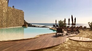 Relax by the pool overlooking the ocean, surrounded by lounge chairs and umbrellas.
