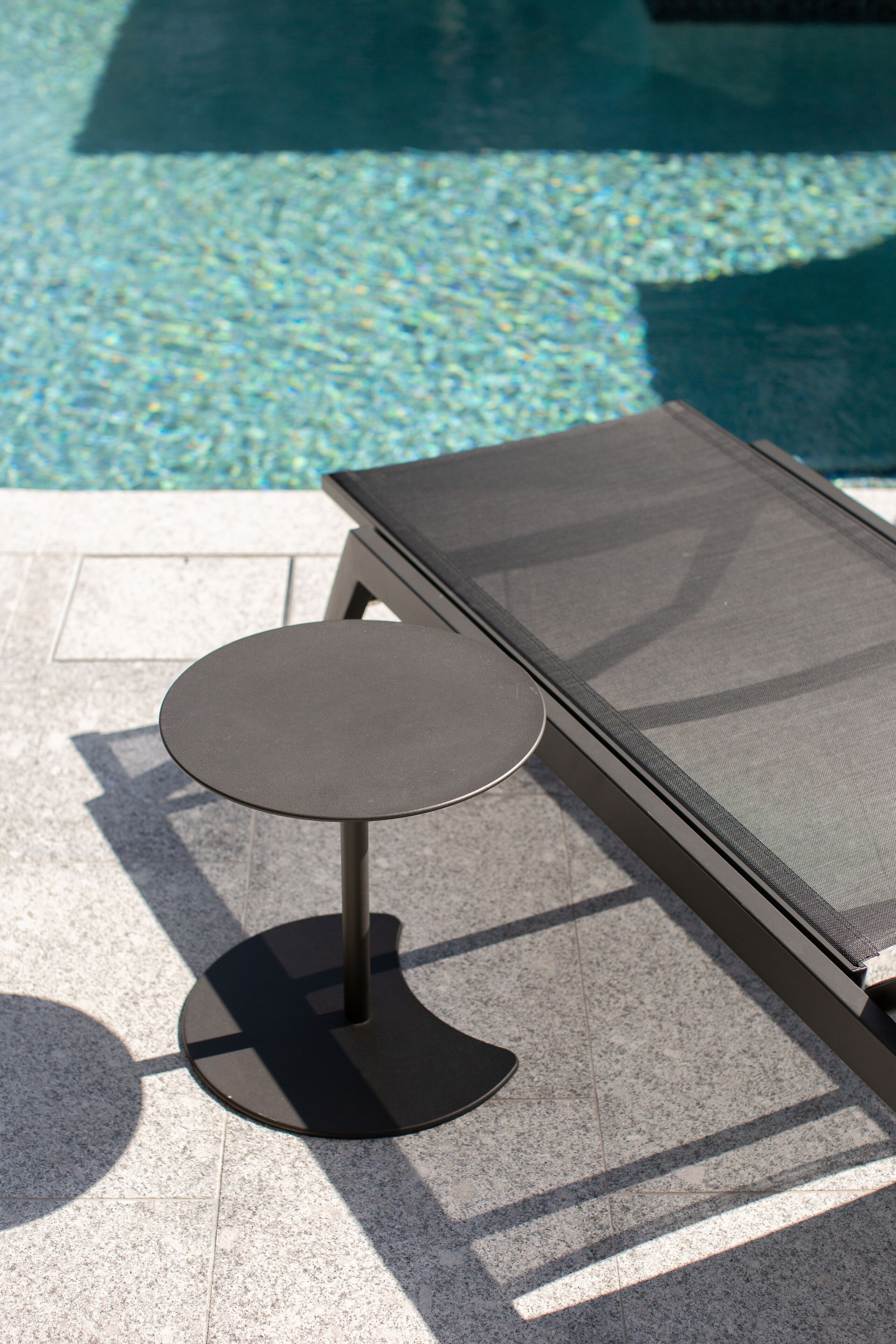 A poolside lounge area with a round table and a sunbed.