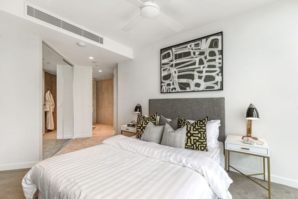 Une chambre moderne avec un grand lit, une tête de lit, une table de chevet avec une lampe et une œuvre d’art abstraite accrochée au mur.