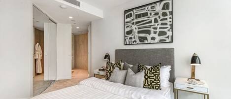 Une chambre moderne avec un grand lit, une tête de lit, une table de chevet avec une lampe et une œuvre d’art abstraite accrochée au mur.