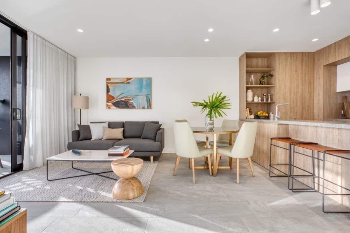 Un salon moderne comprenant un canapé, une table basse et une table à manger. Il y a également un coin cuisine avec un bar et des étagères.