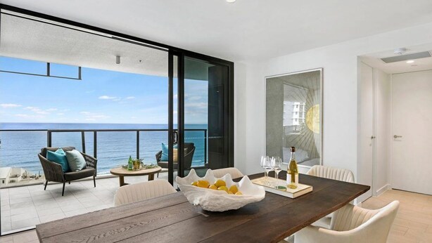 A modern dining area with a wooden table, white chairs, and a view of the sea. - Vue Broadbeach (Broadbeach)
