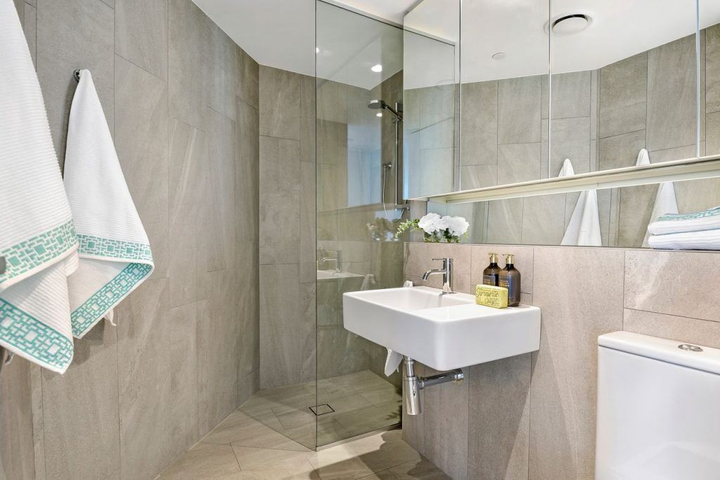 Un baño moderno con ducha envuelta en vidrio, un lavamanos blanco y un inodoro.