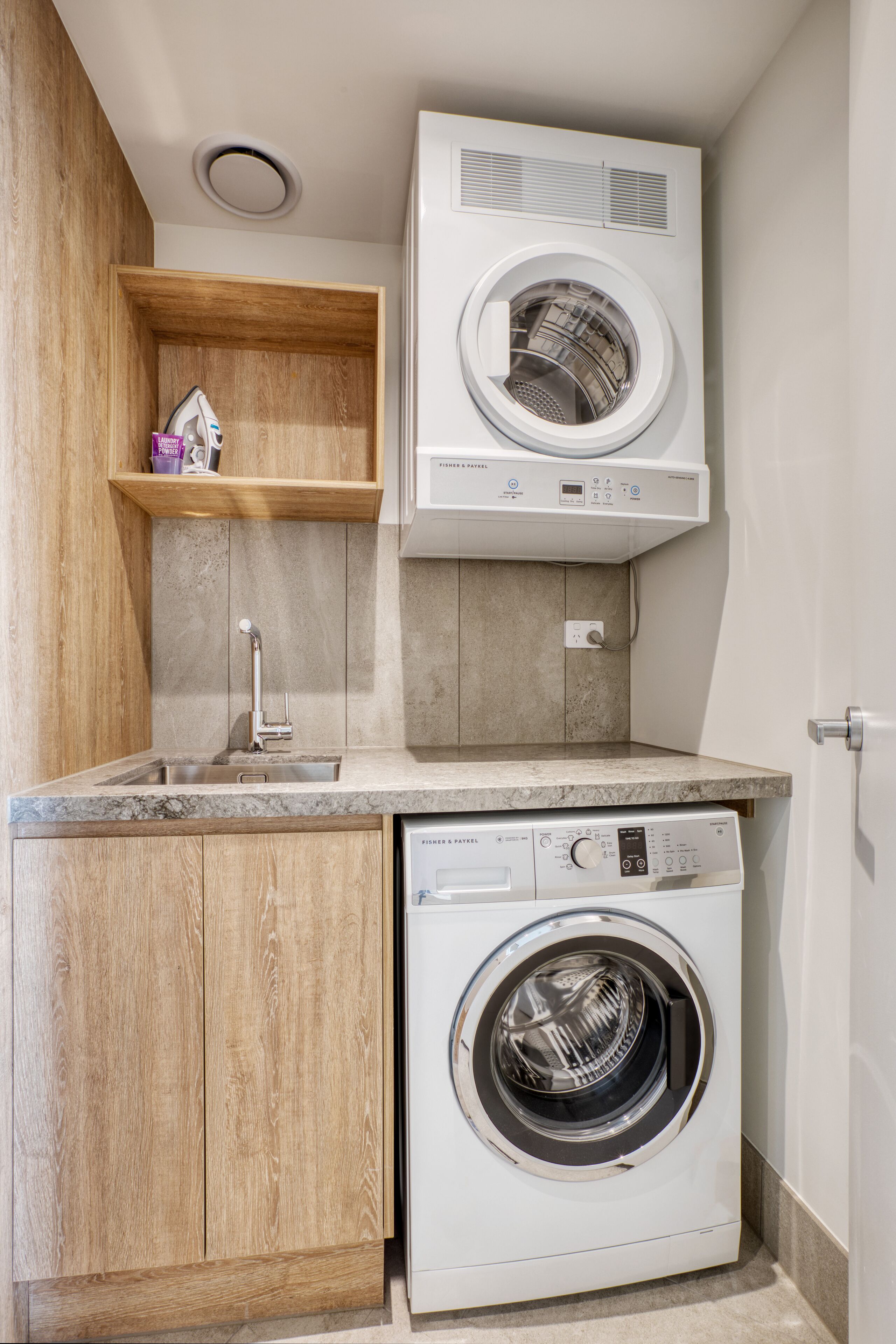 A compact laundry area with a washing machine and dryer, wooden cabinets, and a small shelf with a few items.