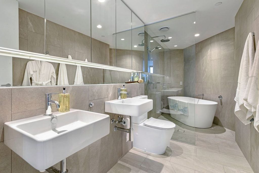 Un baño moderno con un espejo grande, dos lavamanos, un inodoro y una bañera independiente.