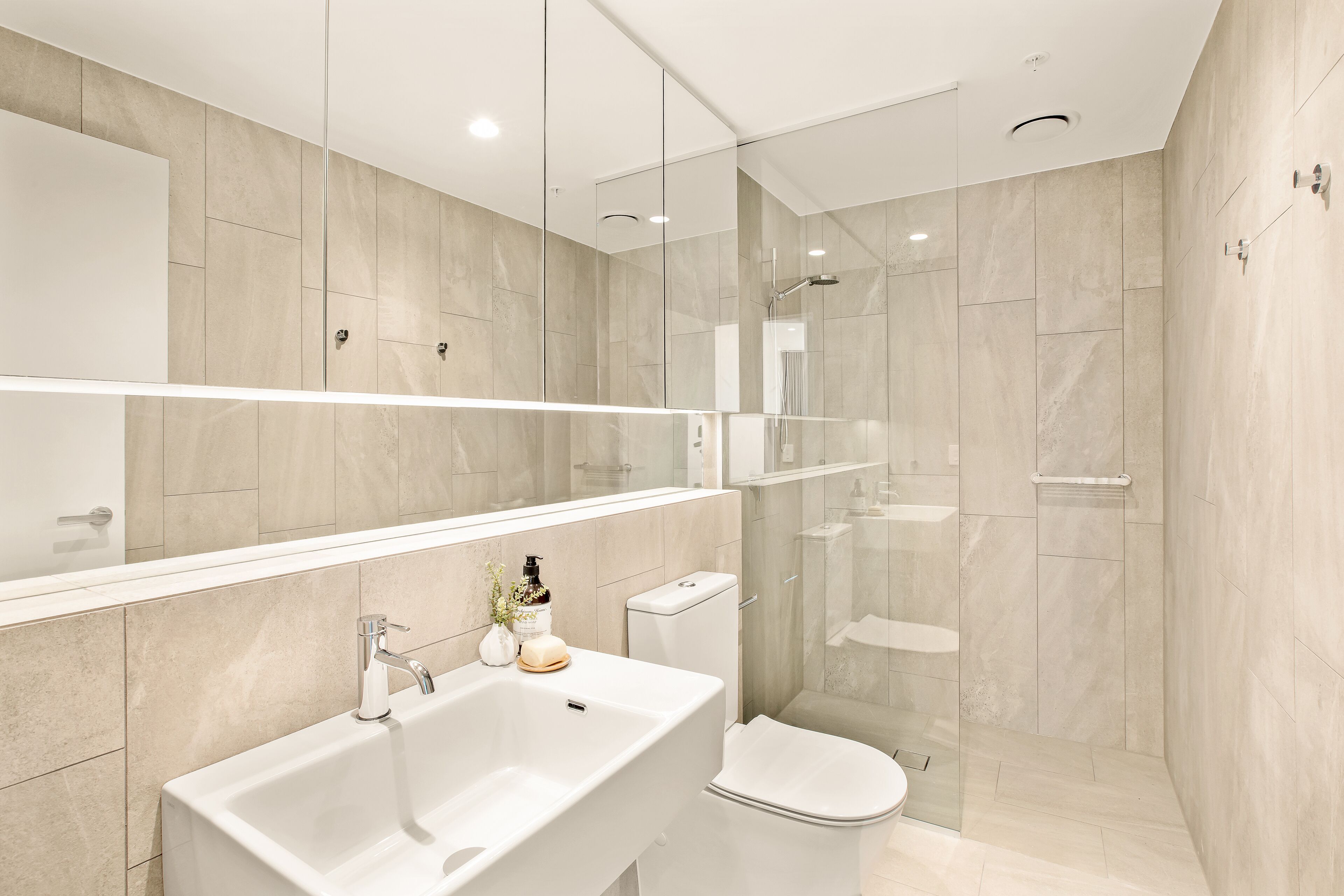 A modern bathroom with a large mirror, a sink, a toilet, and a glass-enclosed shower area.