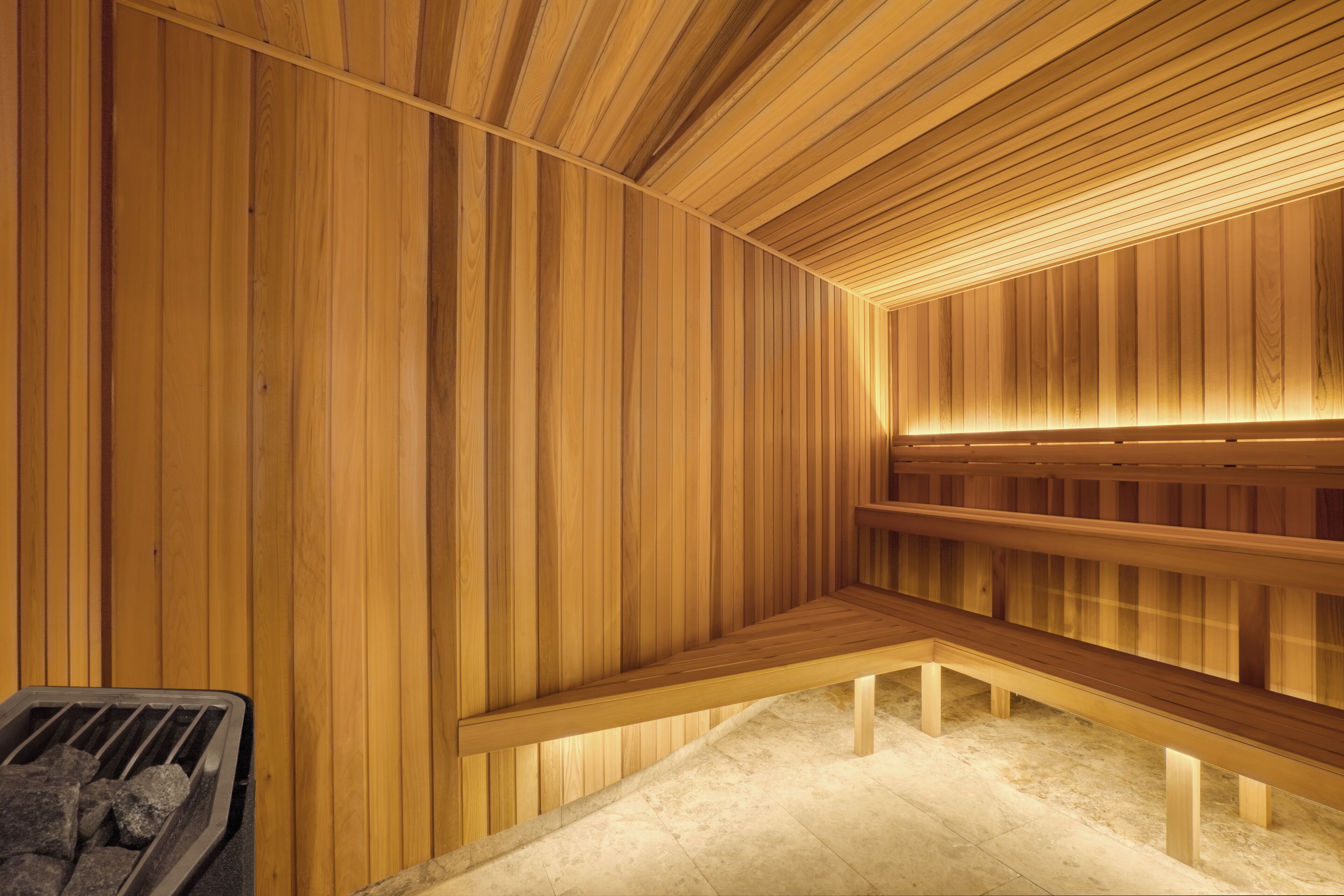 A sauna with wooden walls and benches, a heated floor, and a bench with a tray of stones.