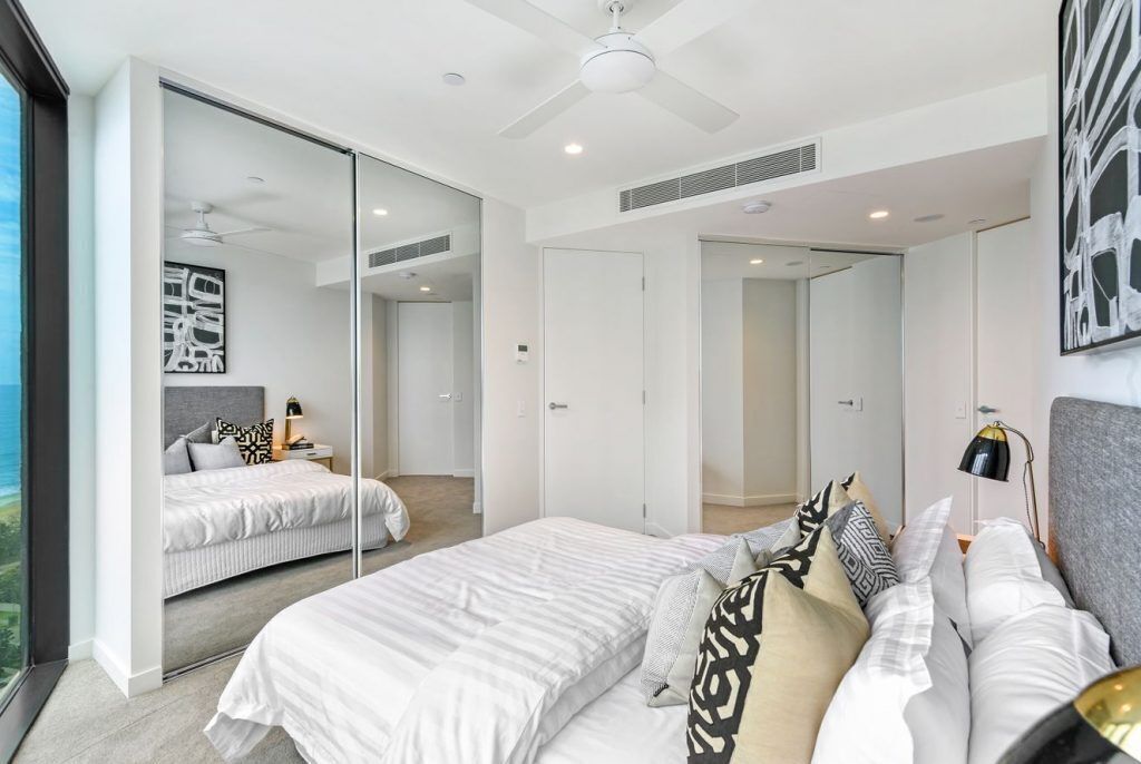 A modern bedroom with a large bed, a ceiling fan, and a view of the outdoors through a sliding door.