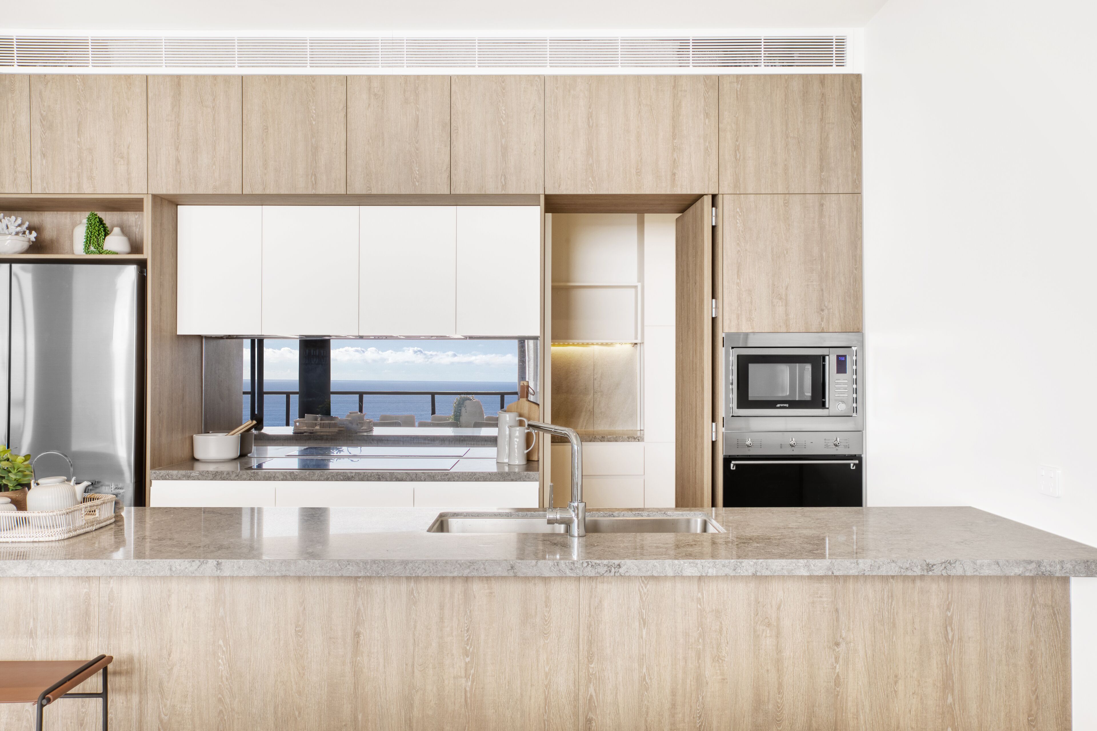 A modern kitchen with a large island, stainless steel appliances, and a view of the ocean.