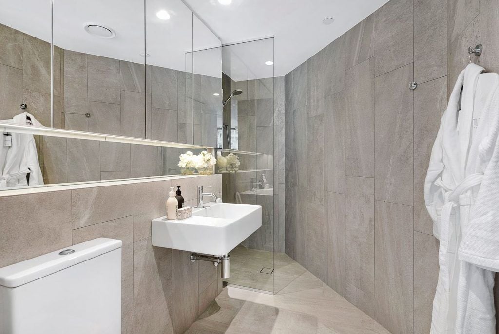 Un baño moderno con ducha de mampara de vidrio, lavamanos blanco y espejo grande.