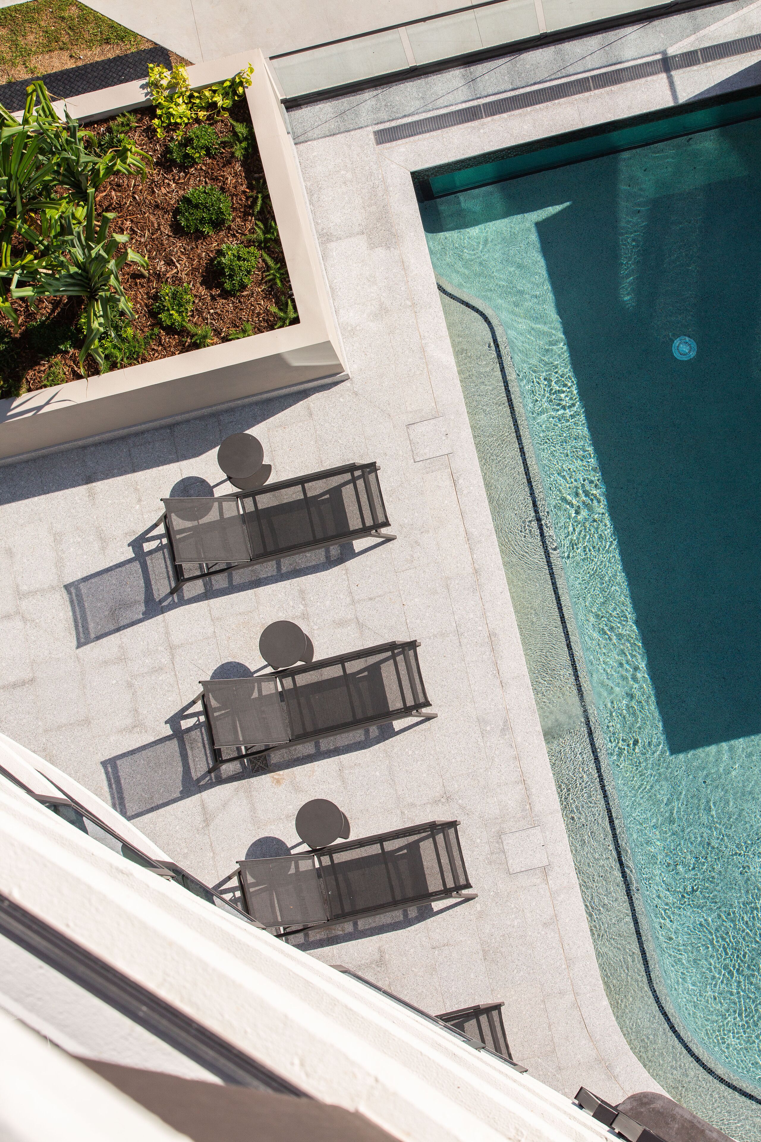 An aerial view of a swimming pool with lounge chairs and a planter with greenery.