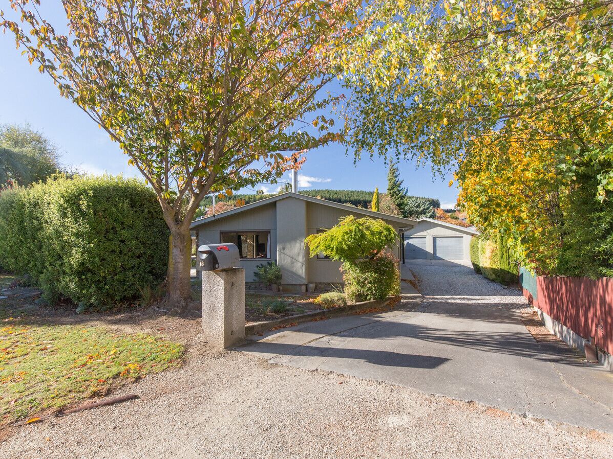 A residential property with a driveway leading to a house, surrounded by mature trees and a well-maintained lawn.