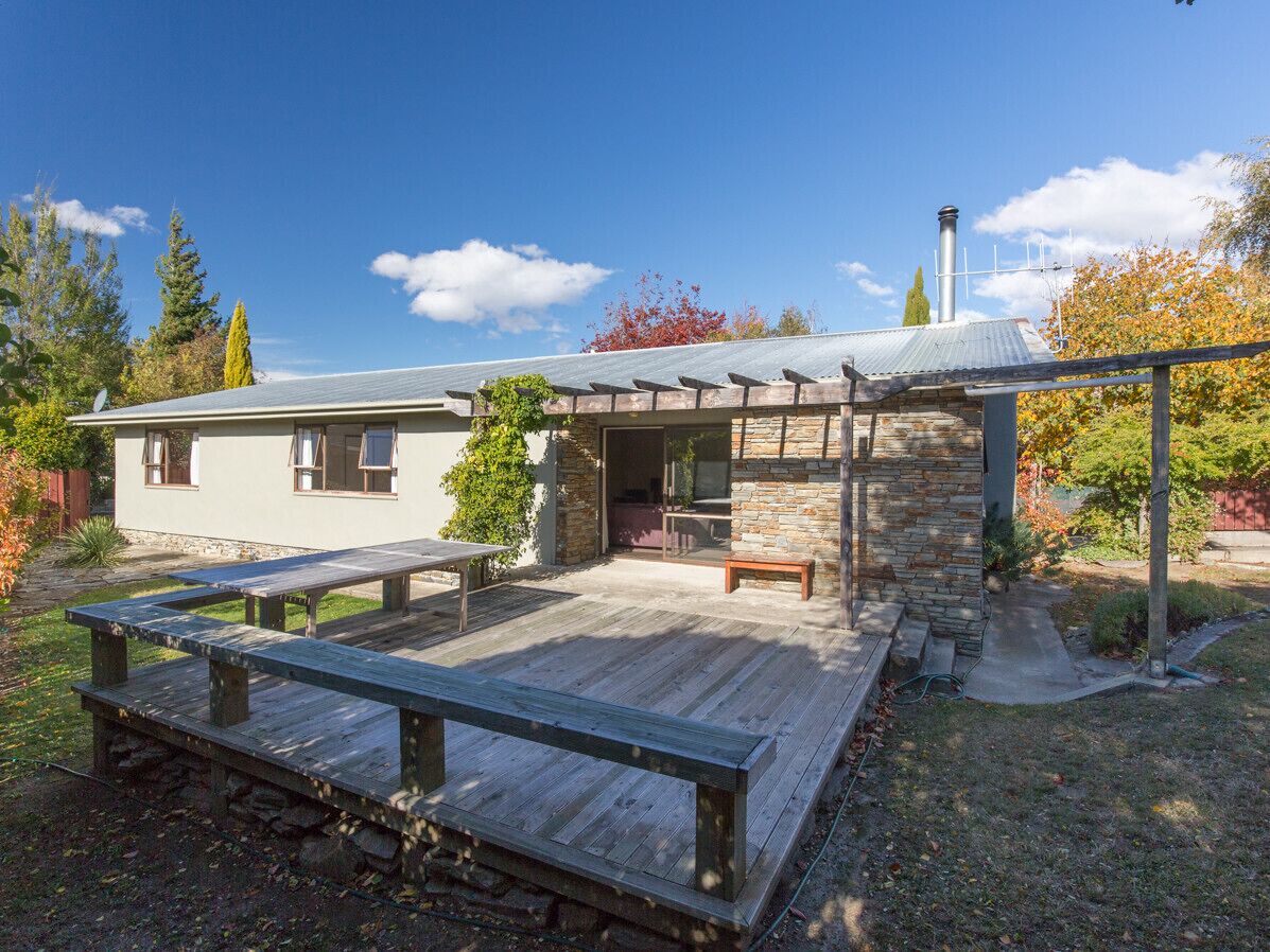 Ein Haus mit einer Terrasse, die Holzbanken und eine Steinstruktur bietet.
