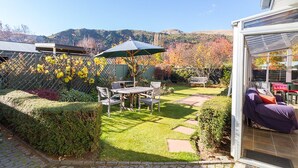 A patio with a table and chairs, a covered seating area, and a view of hills. - Brow Peak View - Arrowtown Holiday Home (Arrowtown)
