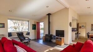 A spacious living room with a red sofa, a black chair, a TV, and a wood-burning stove. - Brow Peak View - Arrowtown Holiday Home (Arrowtown)