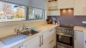 A modern kitchen with a built-in oven, a sink, and a window with blinds. - Brow Peak View - Arrowtown Holiday Home (Arrowtown)